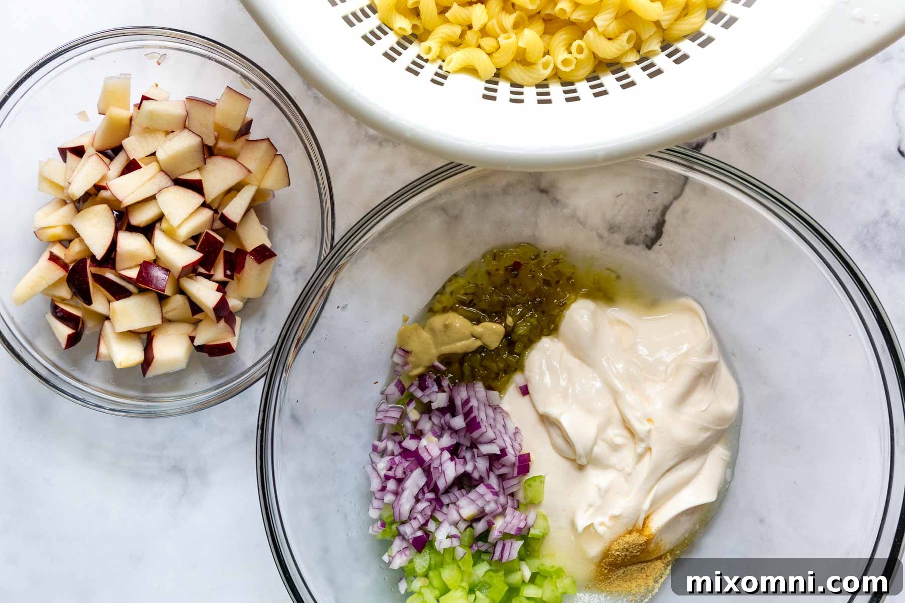 A bowl of cooked gluten-free pasta, chopped apple, and ingredients for the creamy dressing.