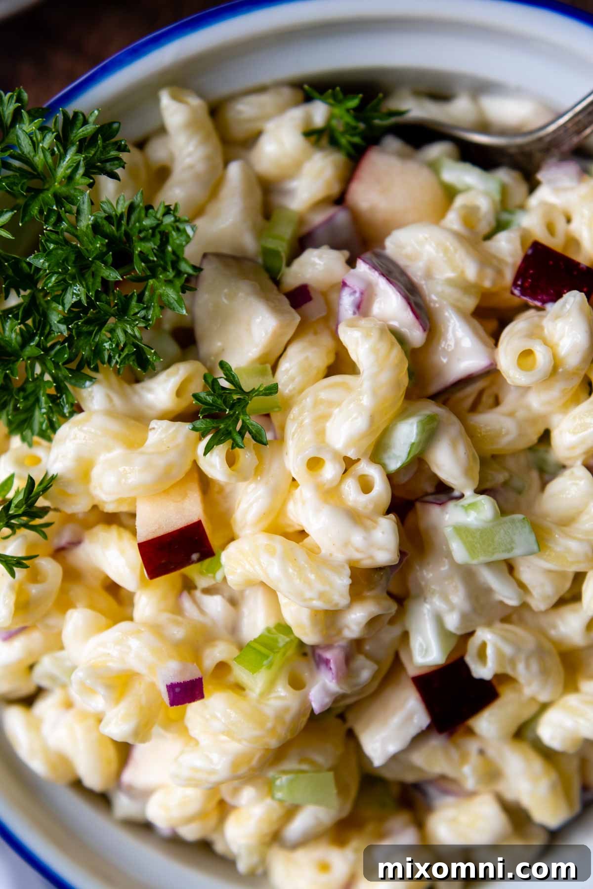 A close-up shot of creamy gluten-free macaroni salad in a white bowl, showing off its texture and ingredients.