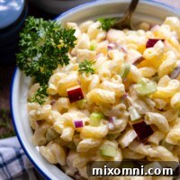 a spoon going into a bowl of macaroni salad with parsley garnish on top.