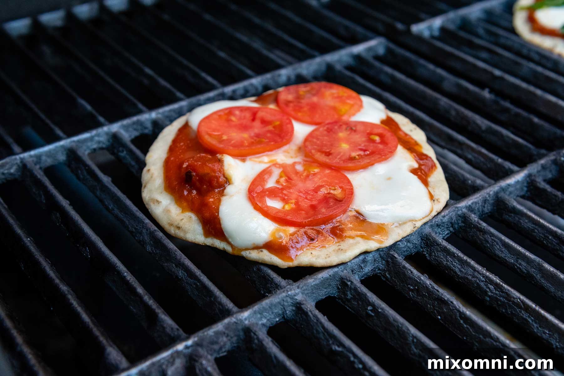 A gluten-free pizza cooking on a grill, adorned with fresh tomatoes and mozzarella cheese.