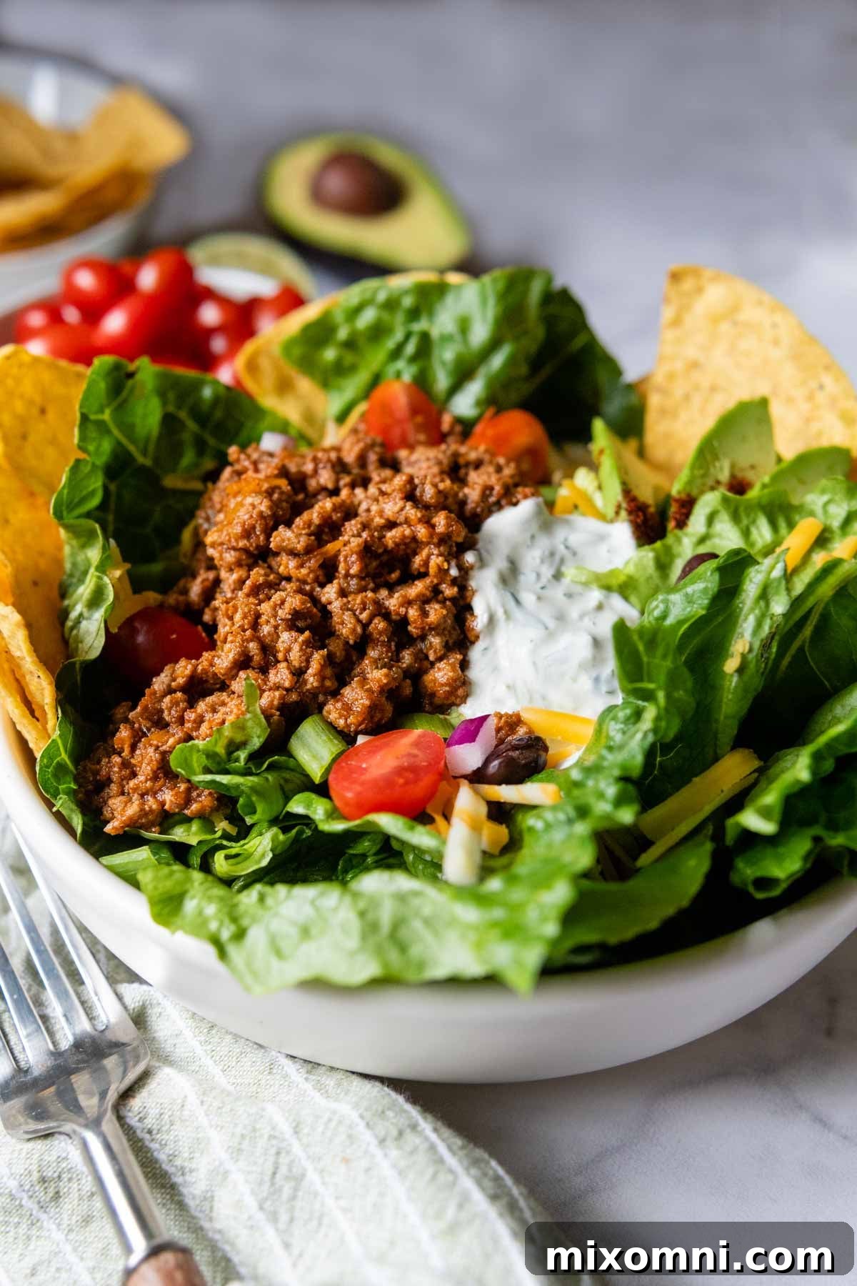 A beautifully arranged gluten-free taco salad in a white bowl, with fresh ingredients like avocado, lime, and cilantro visible in the background, ready to be enjoyed.
