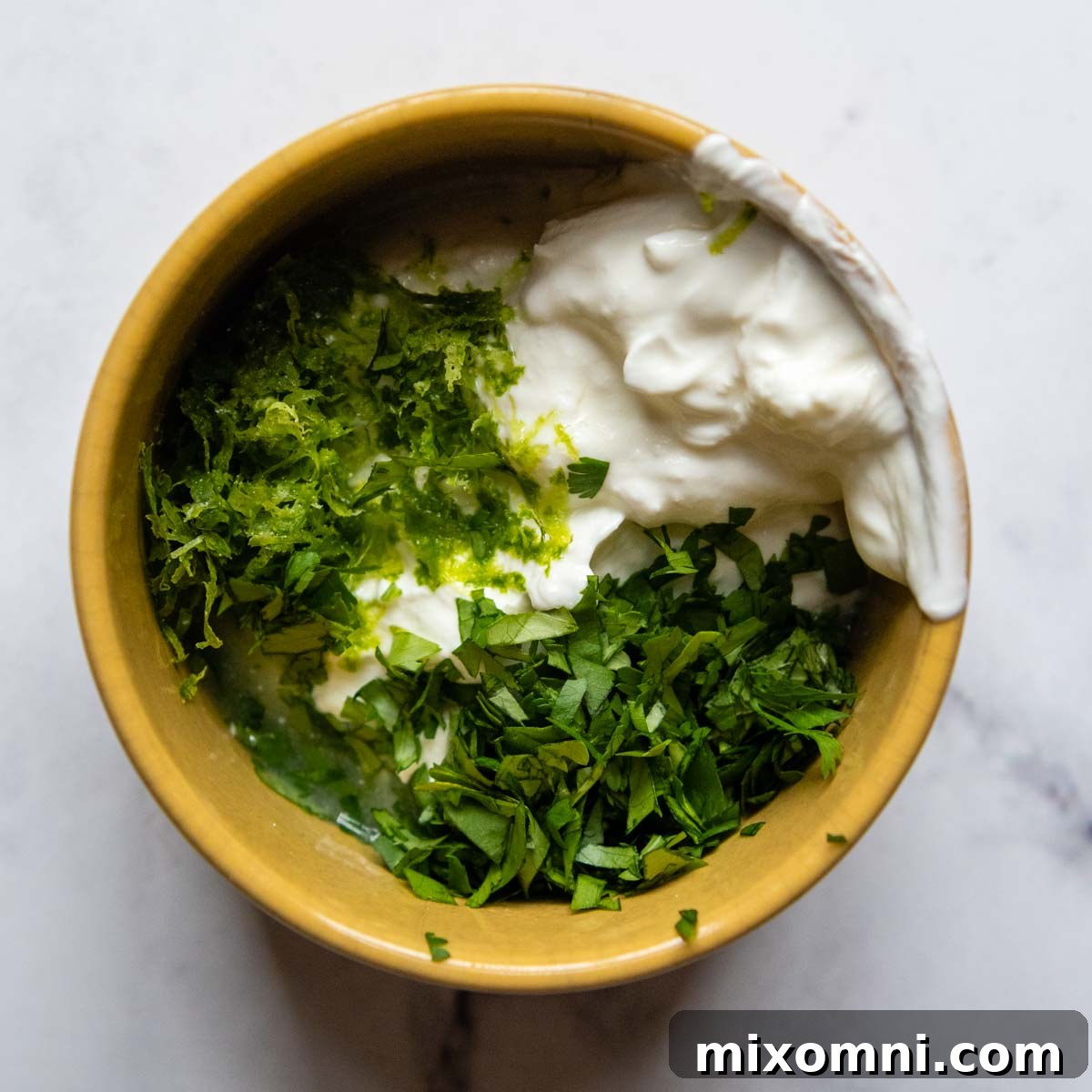 Ingredients for lime cilantro sour cream (sour cream, lime, cilantro) in a small yellow bowl, ready to be mixed.