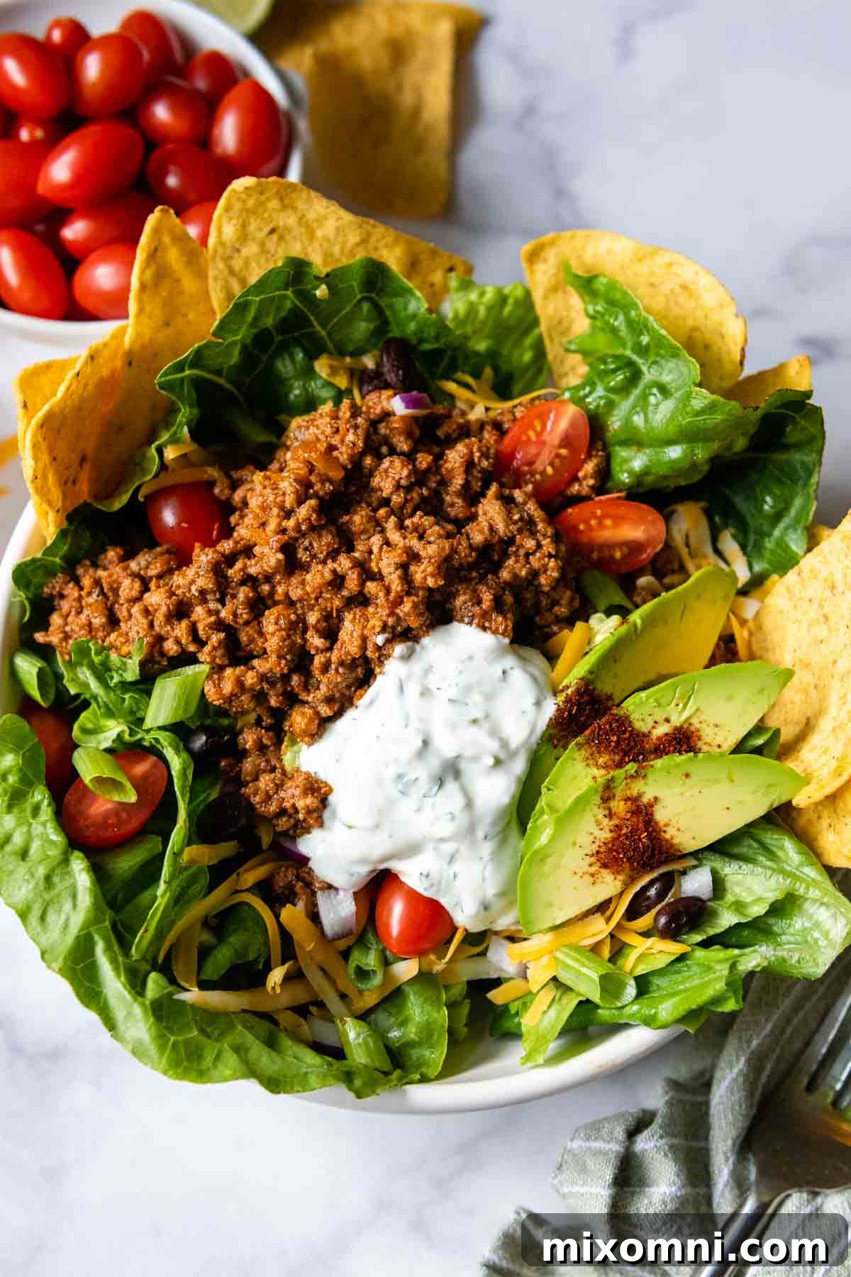 An overhead shot of a vibrant gluten-free taco salad, generously topped with crushed tortilla chips and fresh avocado slices, ready to be served.