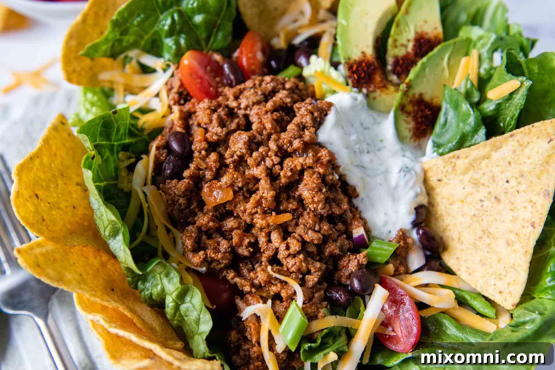A close-up shot of rich, seasoned taco meat beautifully layered on top of a fresh, crisp salad, ready for additional toppings.