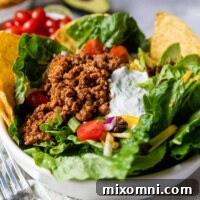 A vibrant and appetizing gluten-free taco salad in a white bowl, with fresh ingredients in the background, making it ready to serve.