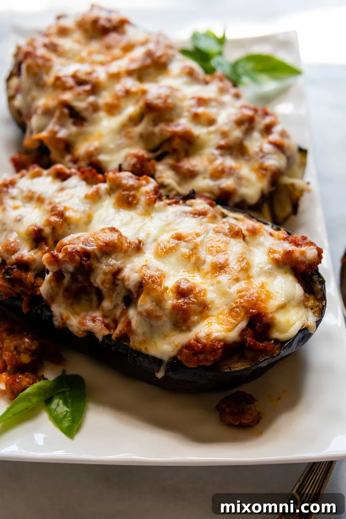 Close-up of golden-brown baked eggplant boats topped with melted cheese and fresh basil, ready to serve on a white dish.