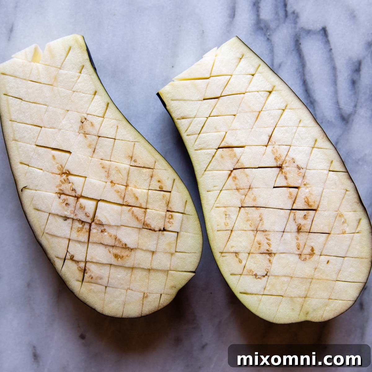 Eggplant halves with crosshatch marks scored into the flesh, ready for seasoning.
