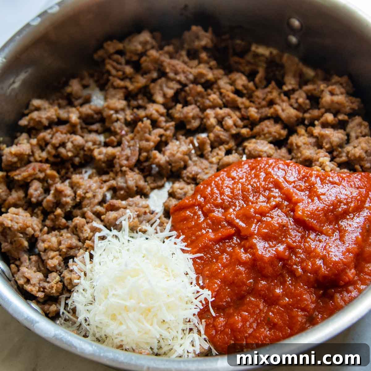 Sweet Italian sausage browning in a skillet with marinara sauce and Parmesan cheese.