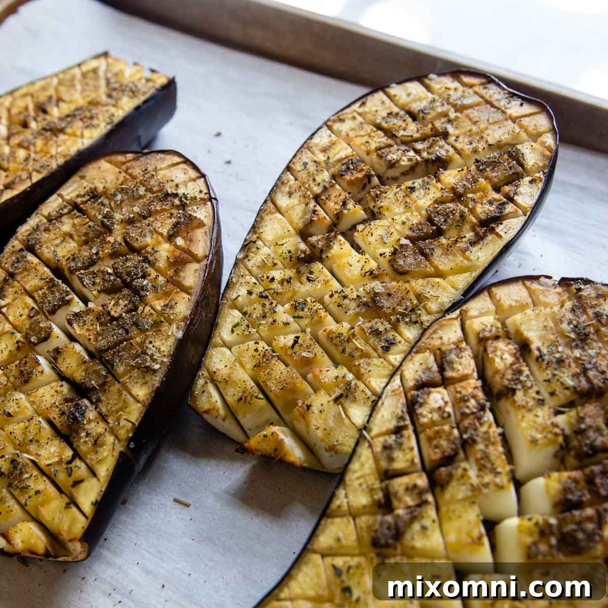 Baked eggplant halves, softened and golden, with the scored lines opened up.