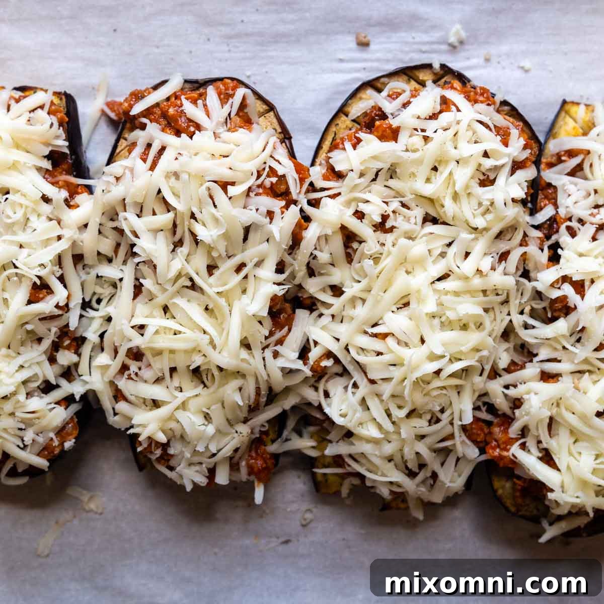 Baked eggplant halves generously topped with the sausage and marinara filling, ready for a layer of mozzarella cheese.