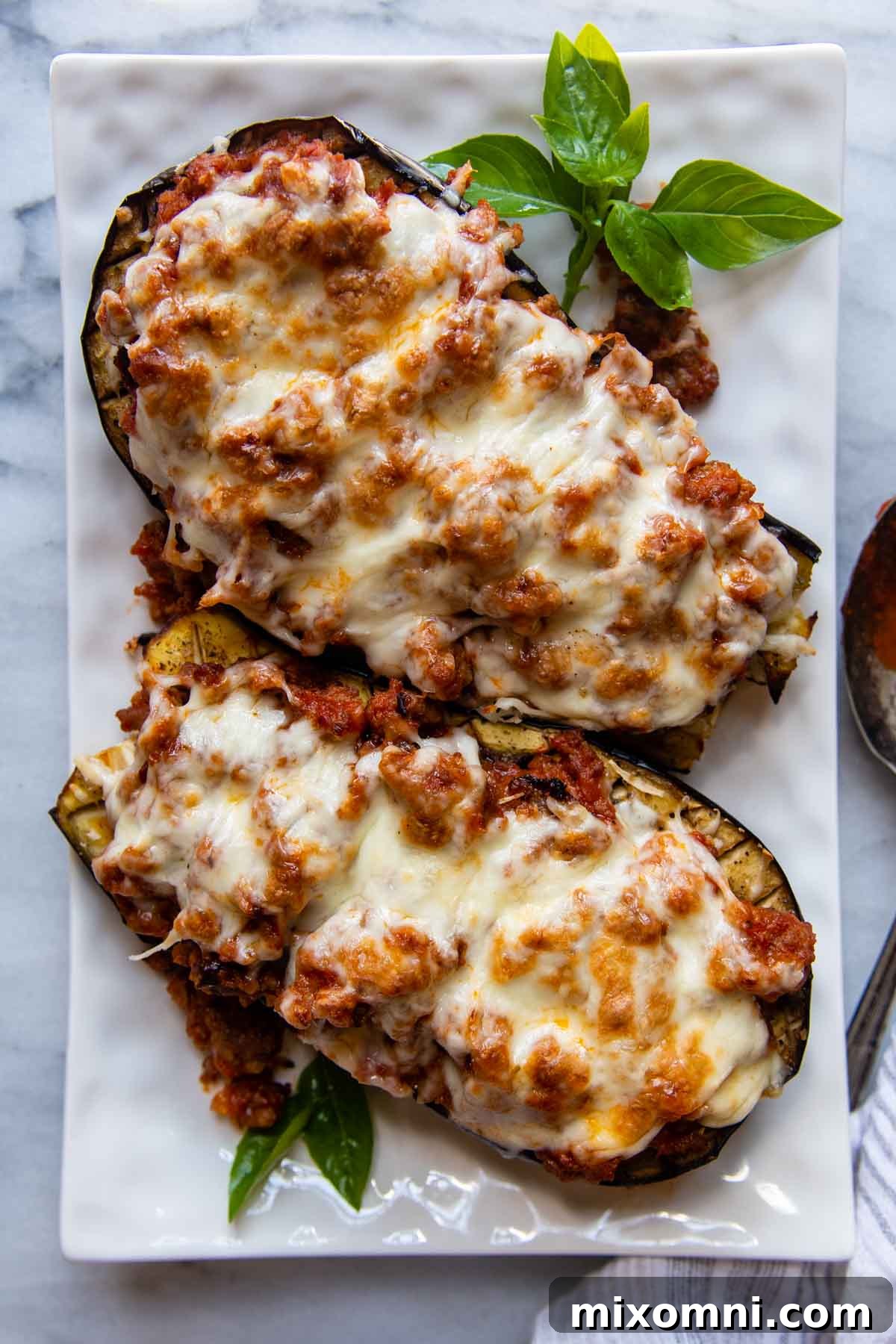 Two beautifully baked eggplant boats, garnished with a fresh basil sprig, presented on a white serving dish.