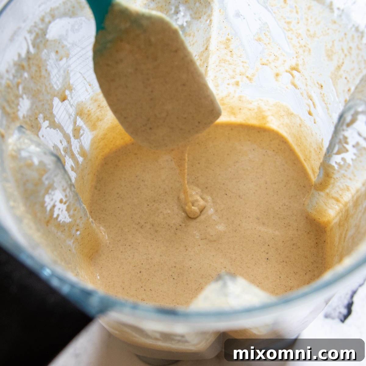 A spoon lifting thickened oat flour pancake batter from a bowl after resting, showing its fluffy consistency.