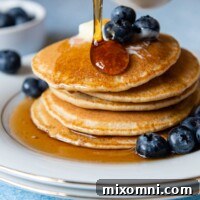 syrup being poured on a stack of pancakes.