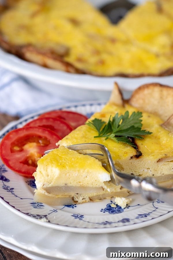 A fork cutting into a bite of potato frittata, with fresh sliced tomatoes resting next to it on a plate.
