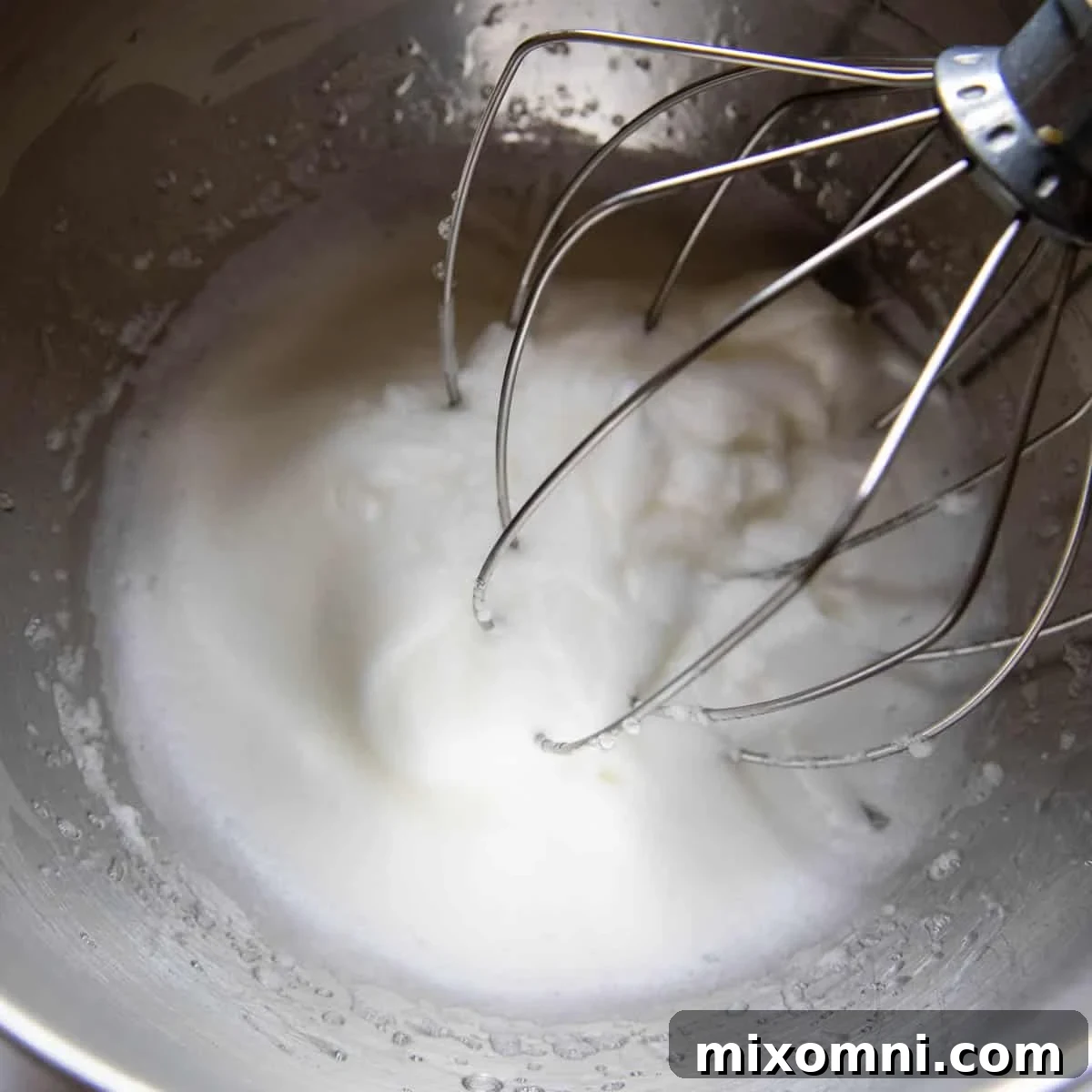 Stiffly beaten egg whites in a metal mixing bowl, ready to be folded into the batter.