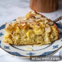 A close-up slice of almond apple cake on a white and blue plate, showing the fluffy interior.