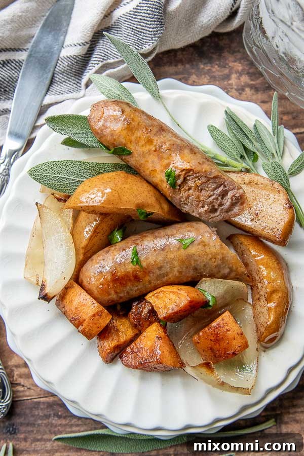 Baked Sausage dinner on a white plate with fresh sage laying next to it, showing a beautifully plated serving.