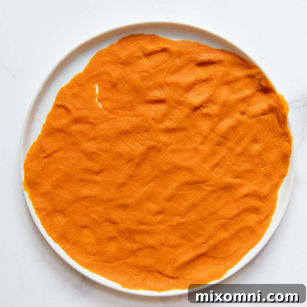 Canned pumpkin puree being spread in a thin layer on a white plate, ready for moisture removal.