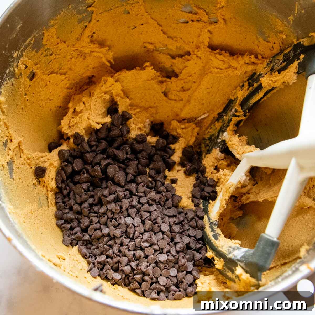 A hand adding a generous amount of chocolate chips into the prepared gluten-free pumpkin cookie dough.