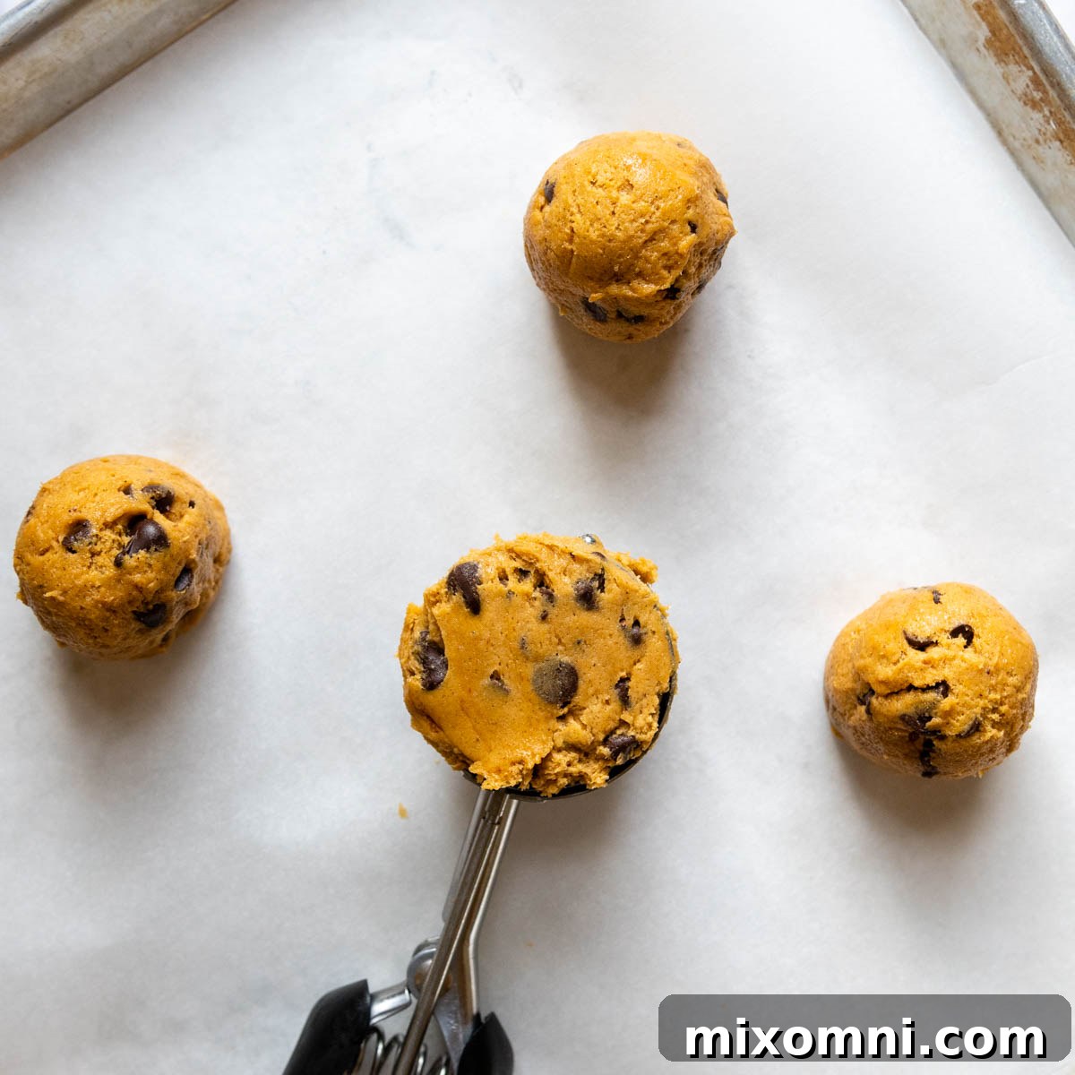 A large cookie scoop portions out gluten-free pumpkin cookie dough onto a parchment-lined baking sheet.