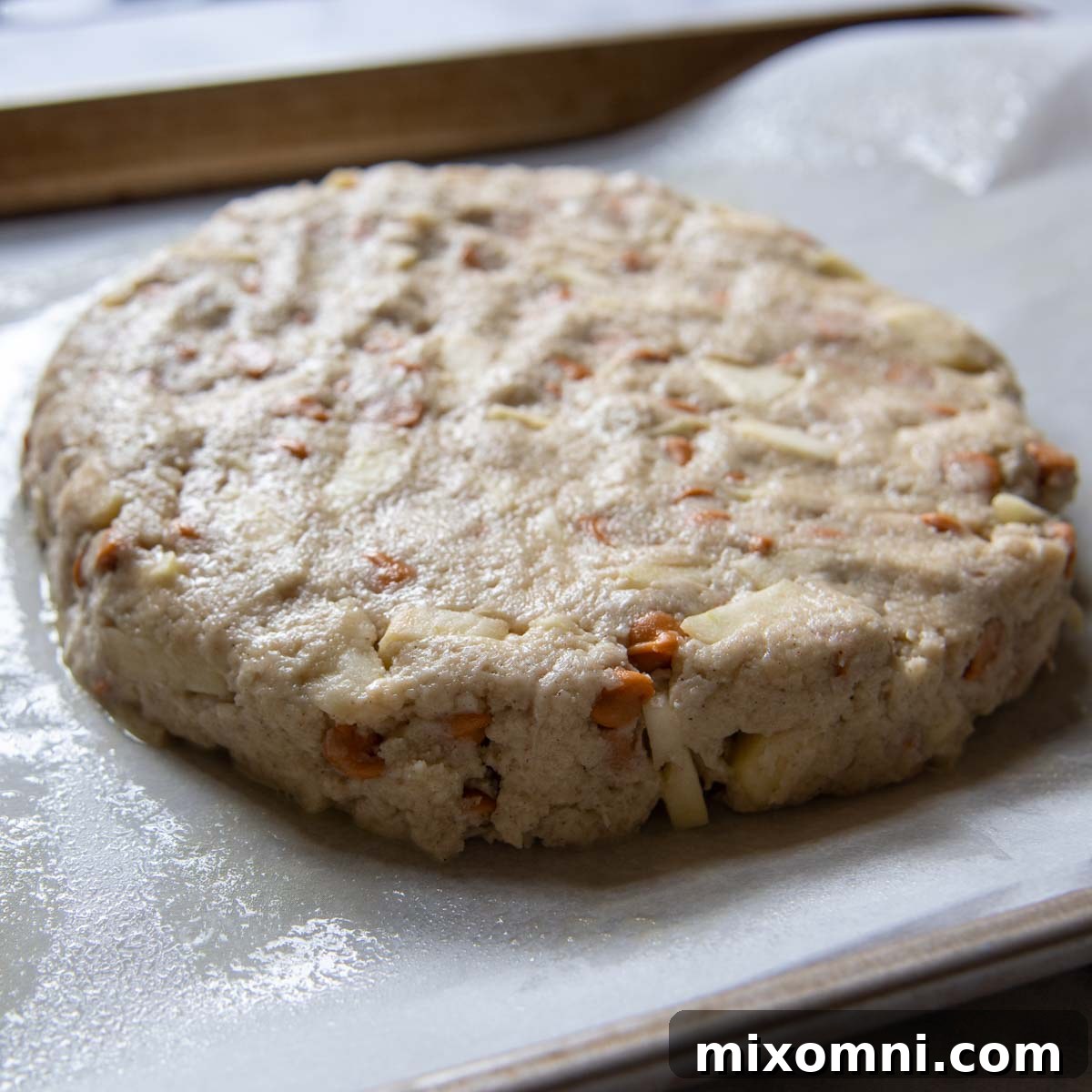 Scone dough shaped into a round disc on parchment paper, ready to be cut.