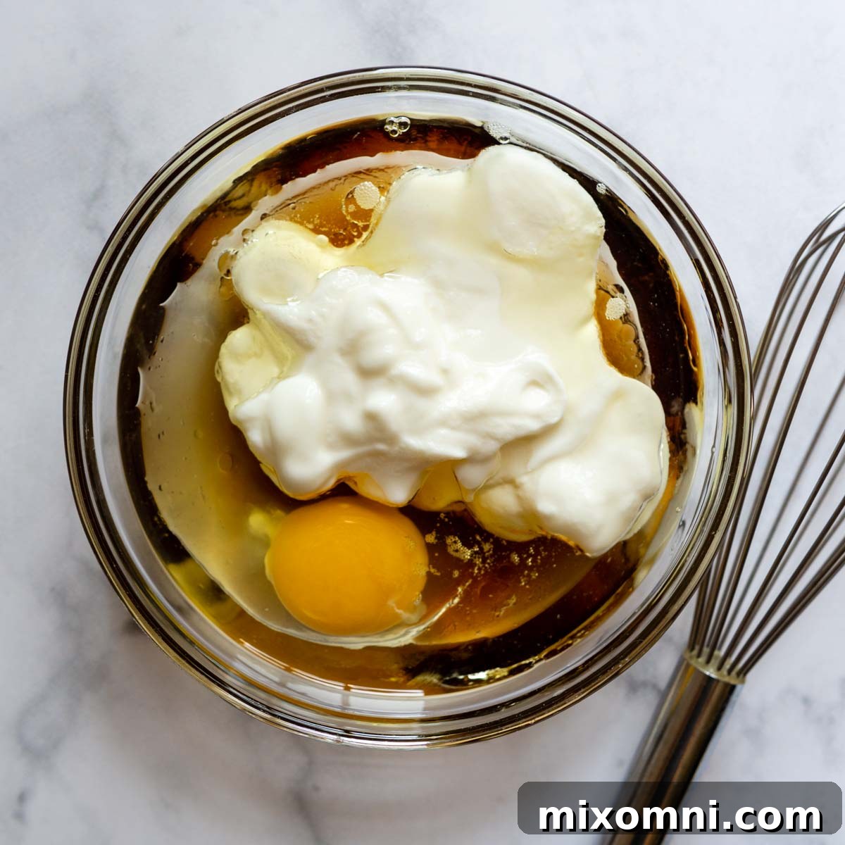 A bowl containing whisked egg, yogurt, oil, and honey, ready to be combined with the dry ingredients.