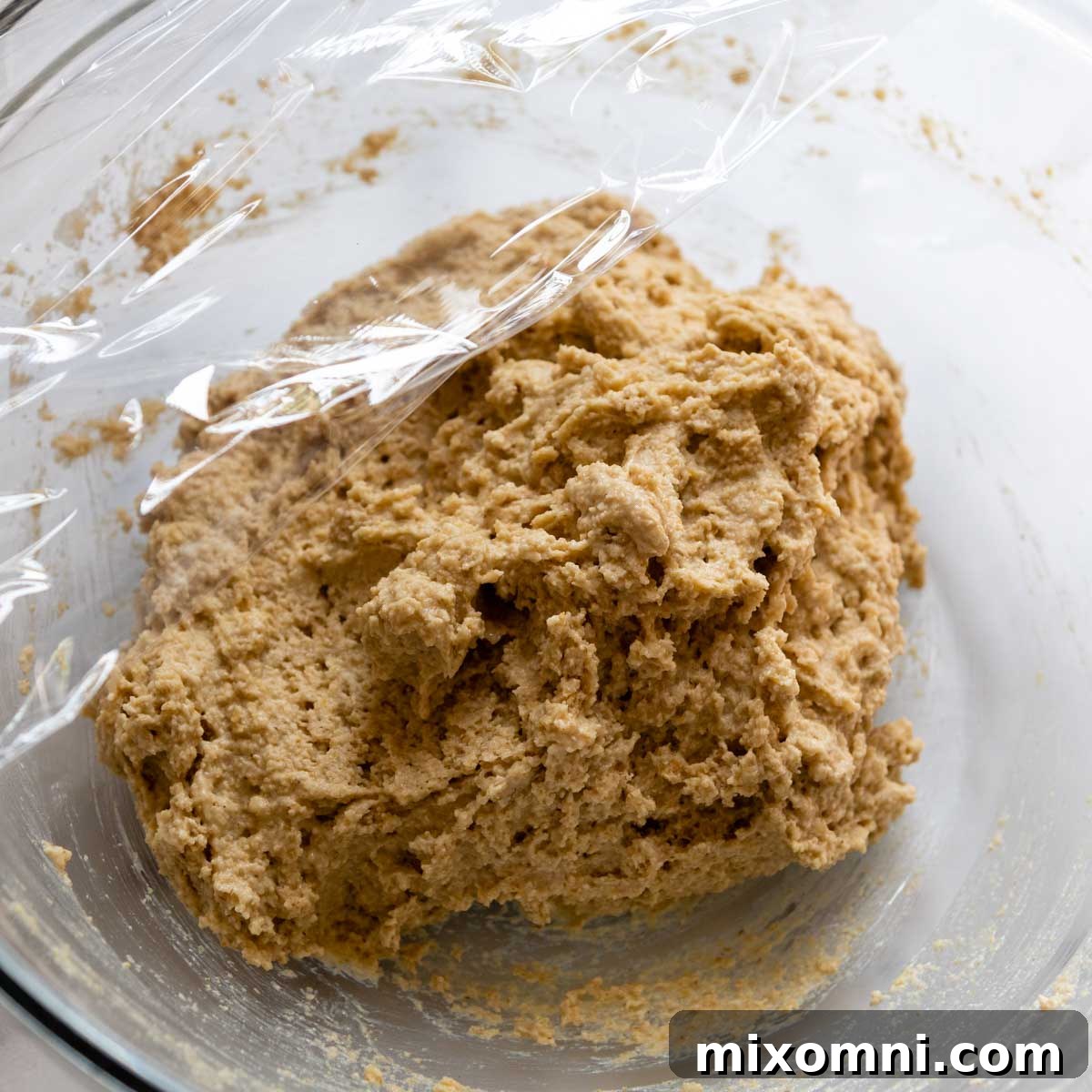 Oat flour biscuit dough resting in a bowl, covered with plastic wrap, indicating the chilling step.