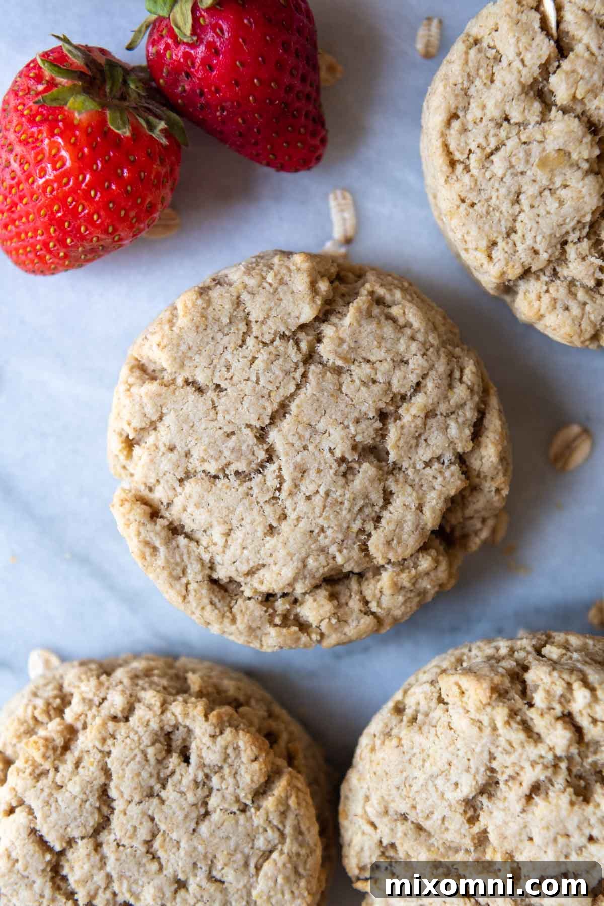 An inviting overhead shot of freshly baked oat flour biscuits arranged on a baking sheet, with vibrant strawberries placed alongside.