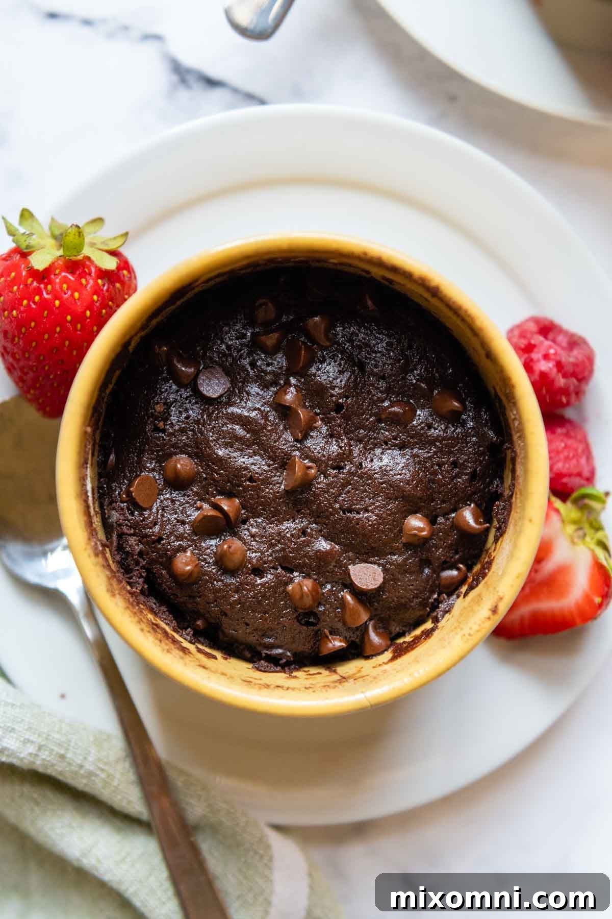 Overhead shot of a delicious gluten-free mug brownie served in a yellow mug, garnished with fresh berries on the side.
