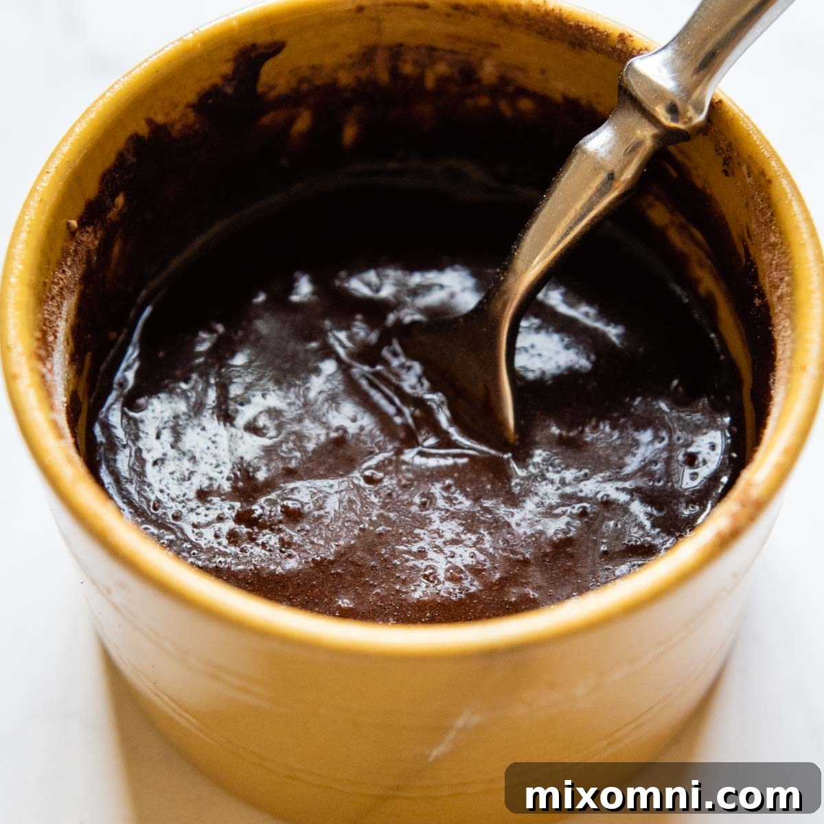 A fork is mixing the brownie batter in a mug, ensuring all dry ingredients are incorporated into the wet mixture.