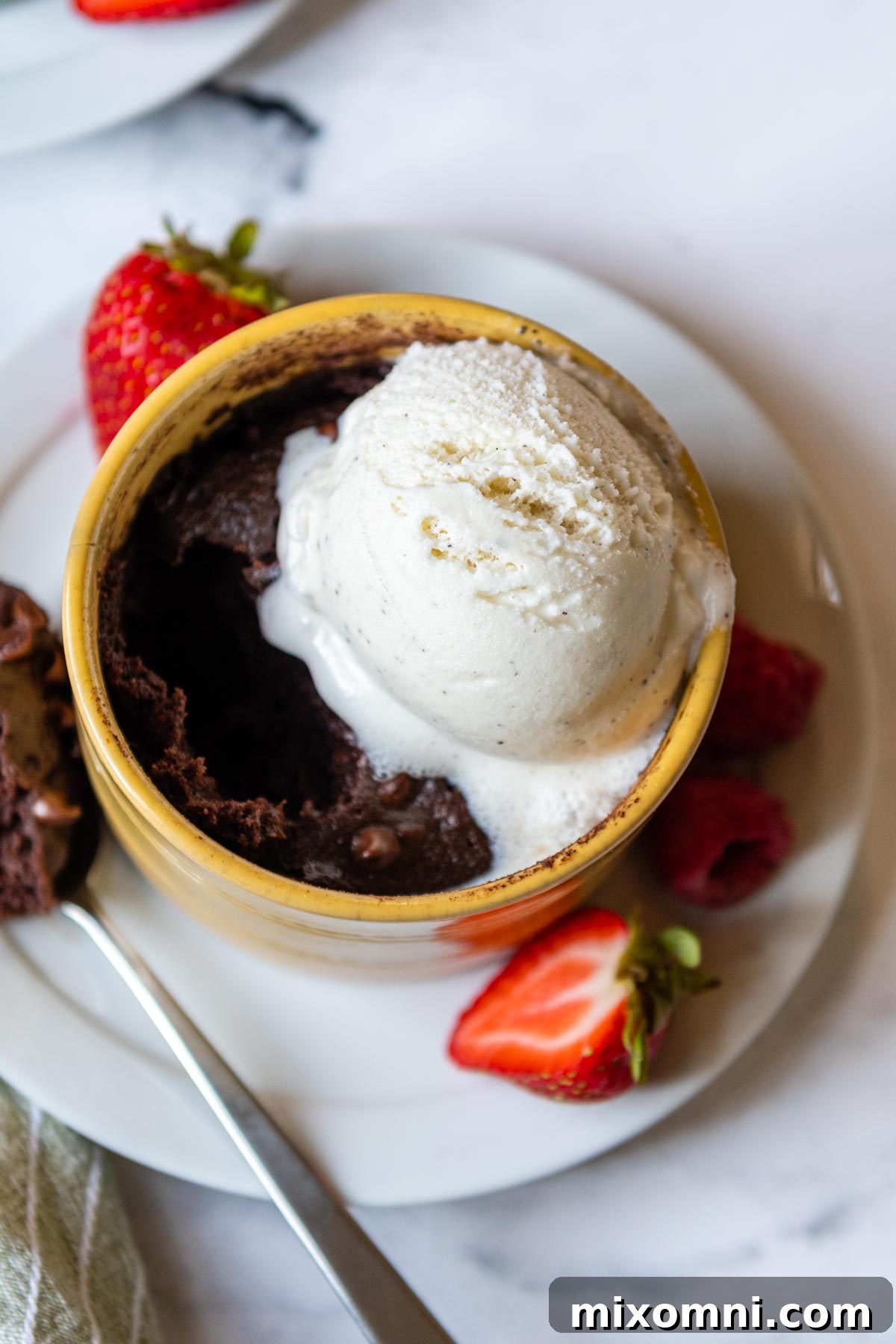 Melting vanilla ice cream cascading over a warm, gooey gluten-free mug brownie, creating a decadent dessert.