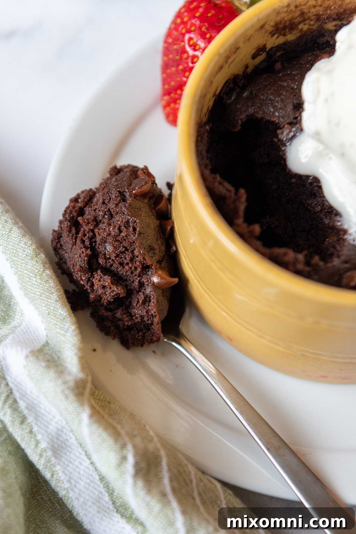 A spoon with a scoop of gluten-free mug brownie resting delicately on the edge of a yellow dish.
