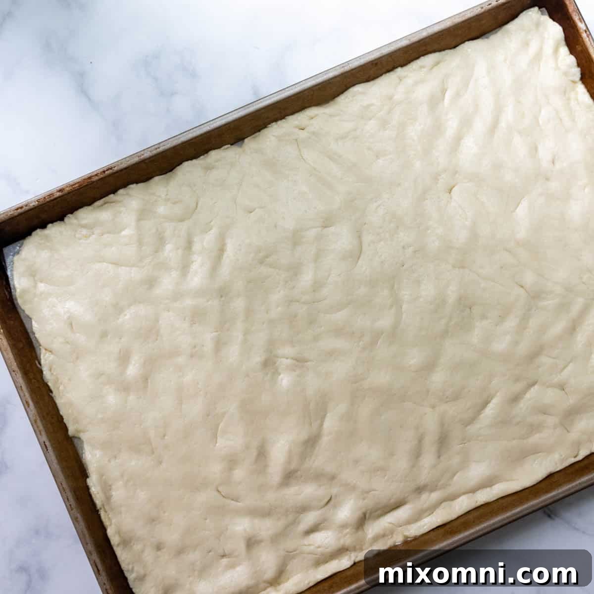 Gluten-free pizza dough evenly patted out onto a parchment-lined baking sheet, forming a large rectangle.