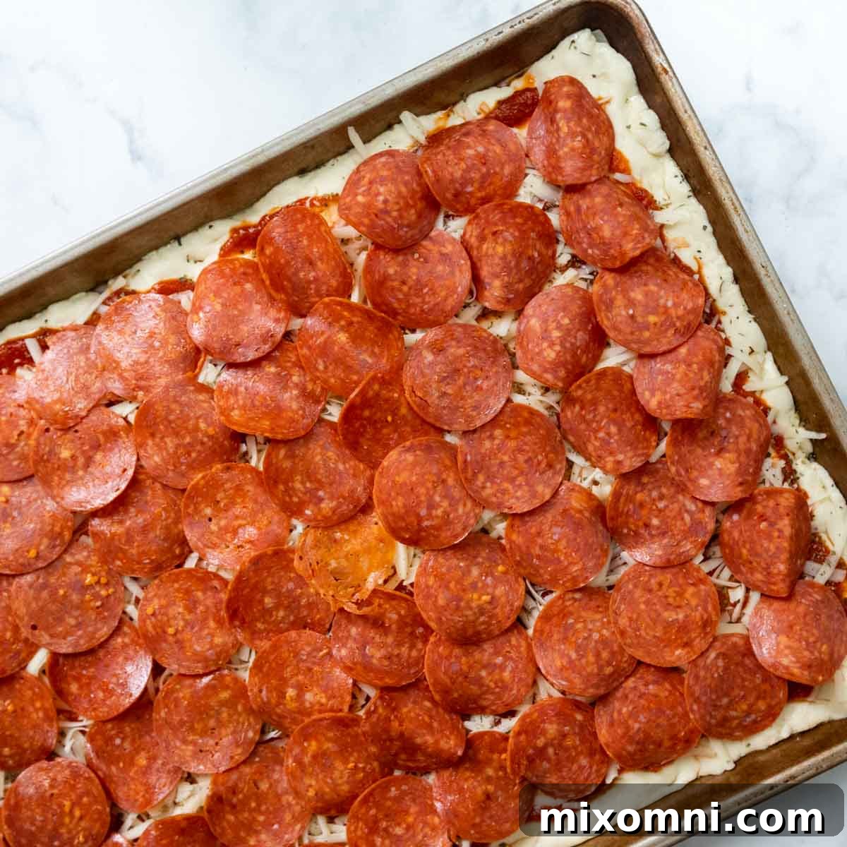 A layer of pepperoni slices neatly arranged on top of the cheese and sauce, covering the gluten-free pizza dough.