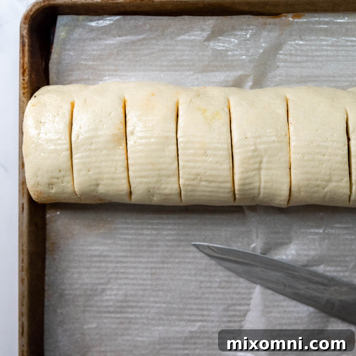 A rolled gluten-free pizza dough log, scored with a knife to indicate where to cut into individual pizza rolls.
