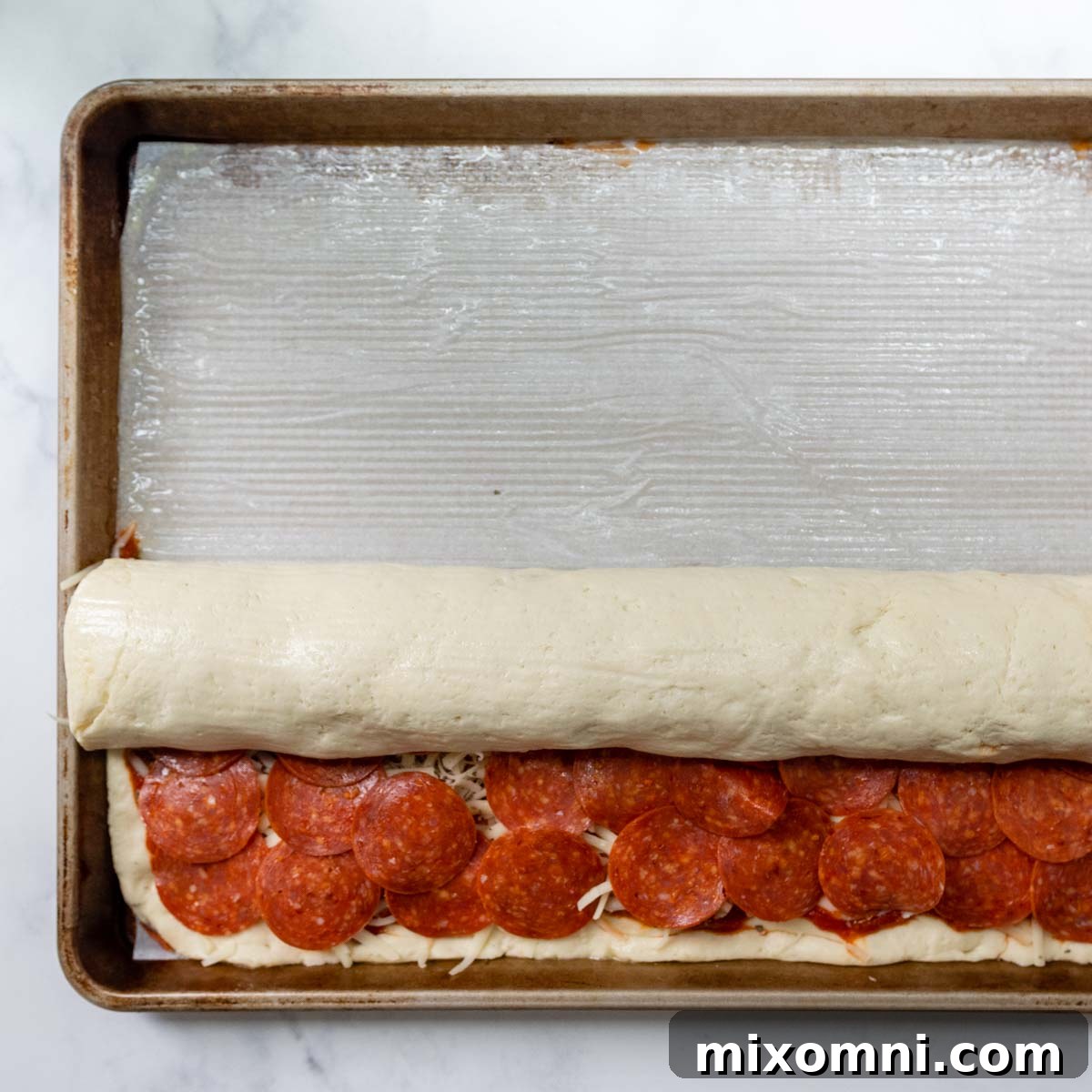 Partially rolled gluten-free dough log on a baking sheet, with a small portion of the dough still unrolled at the near edge.