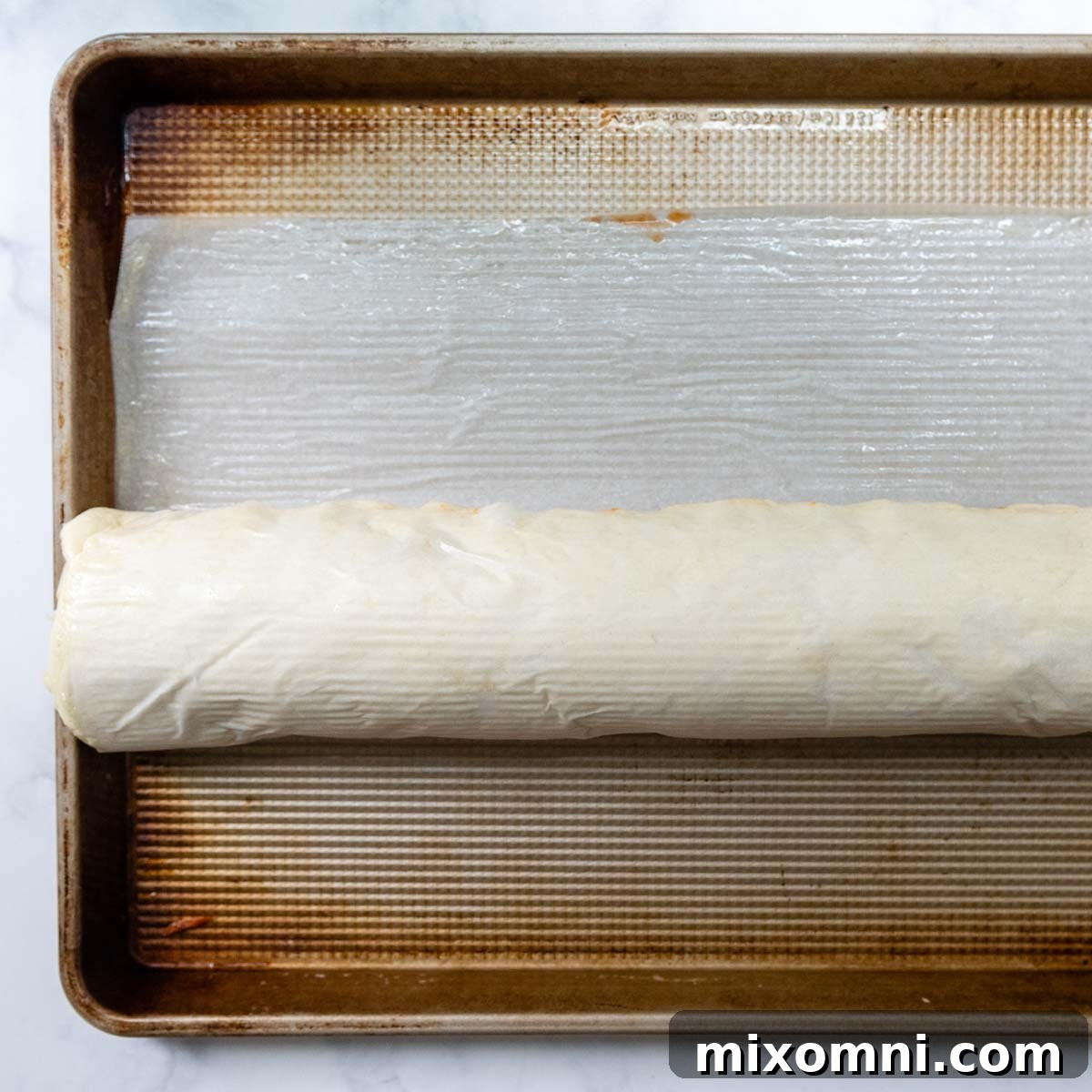 The fully rolled gluten-free pizza log, with parchment paper used to secure the seam face down on the baking sheet.