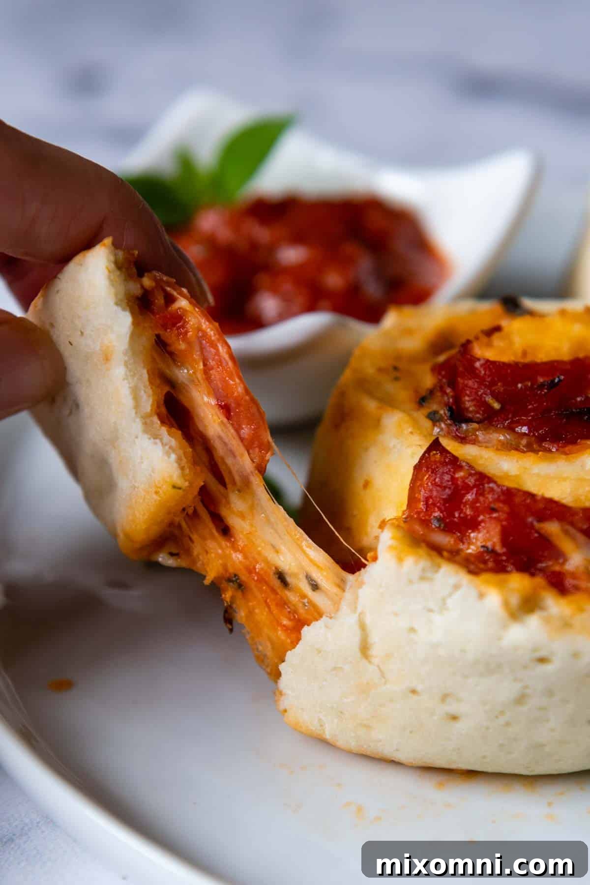 A close-up shot of a gluten-free pizza roll being pulled apart, revealing gooey melted cheese and savory pepperoni inside.