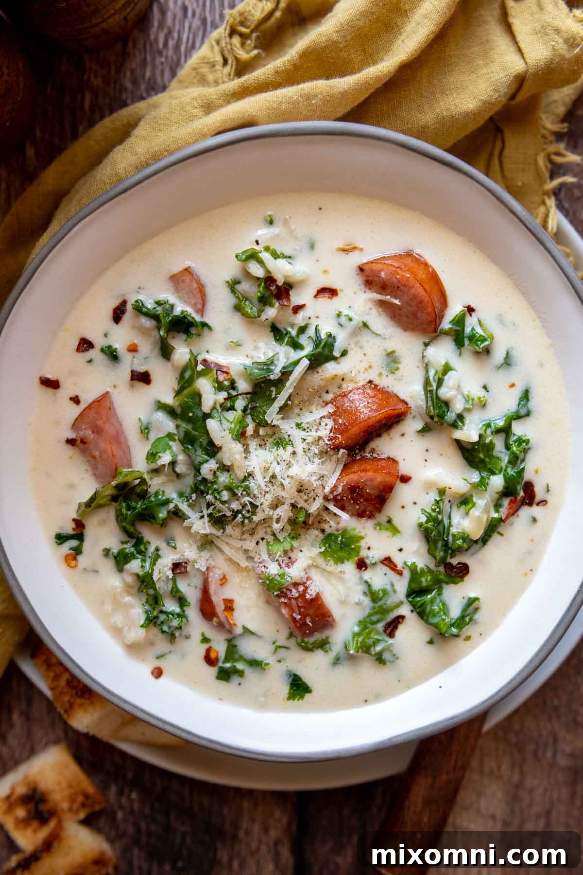 overhead shot of kale soup with sausage in a white bowl and yellow napkin next to it.