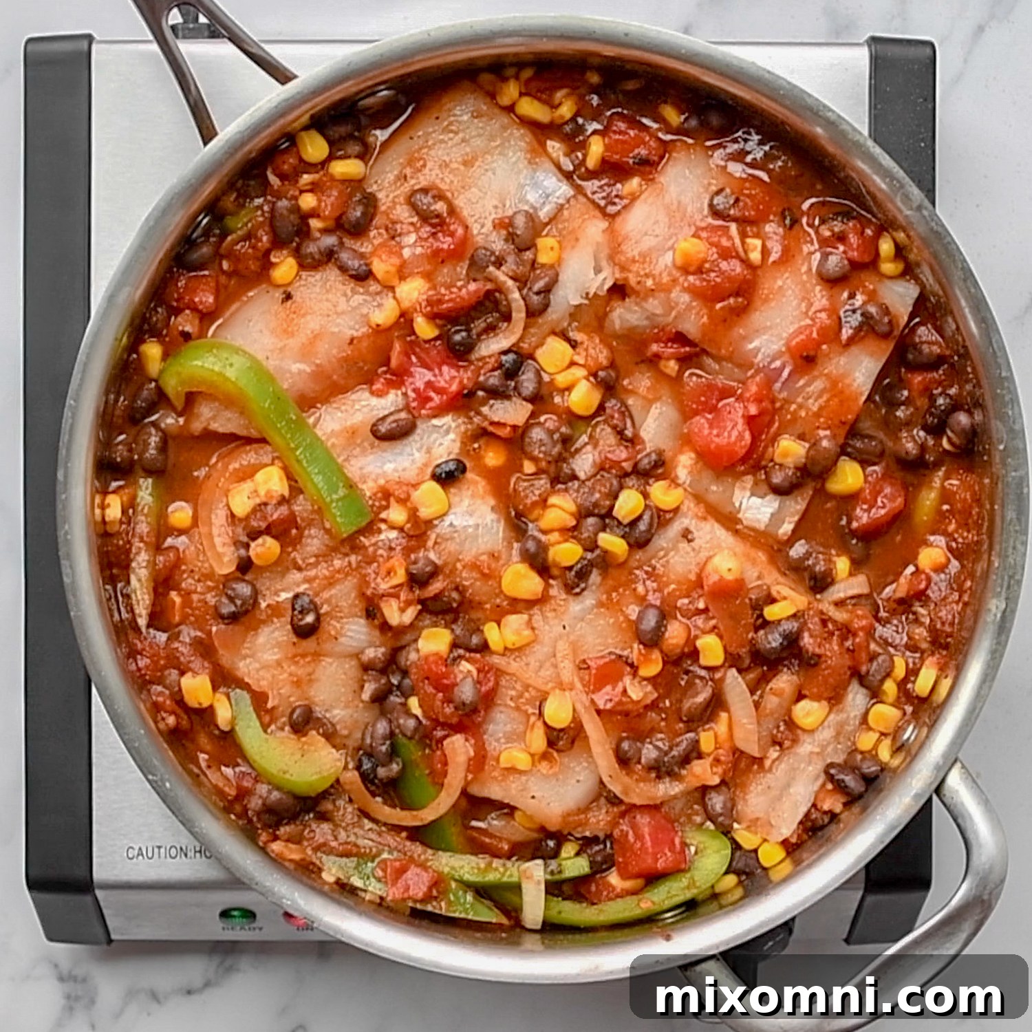 White fish simmering in a vibrant Mexican sauce within a skillet.