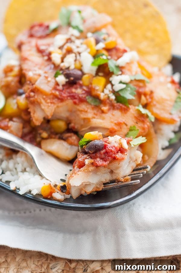 A fork with a bite of Mexican fish, resting on a black plate with rice.