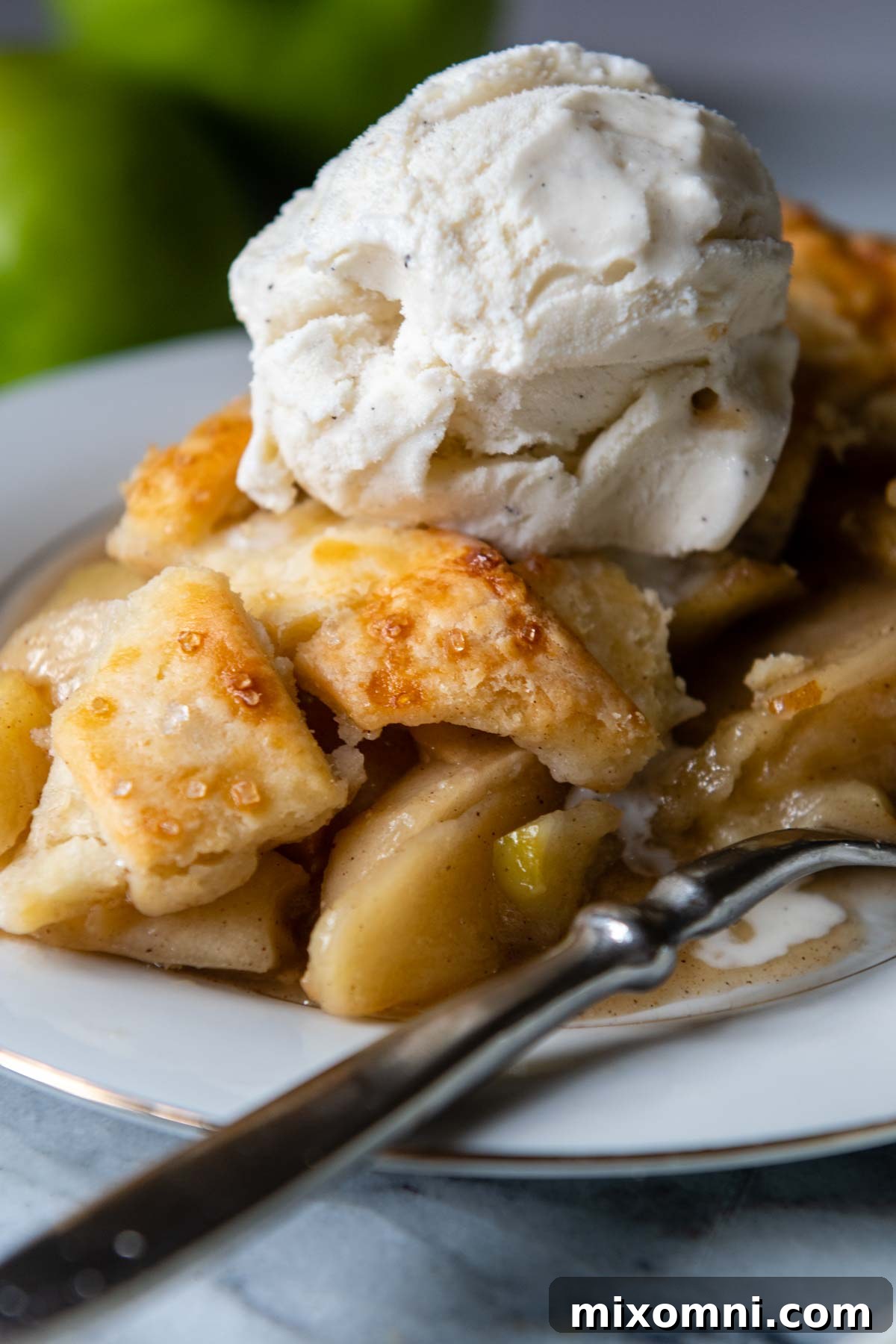 A glorious slice of gluten-free apple pie on a white plate, topped with a scoop of vanilla ice cream.