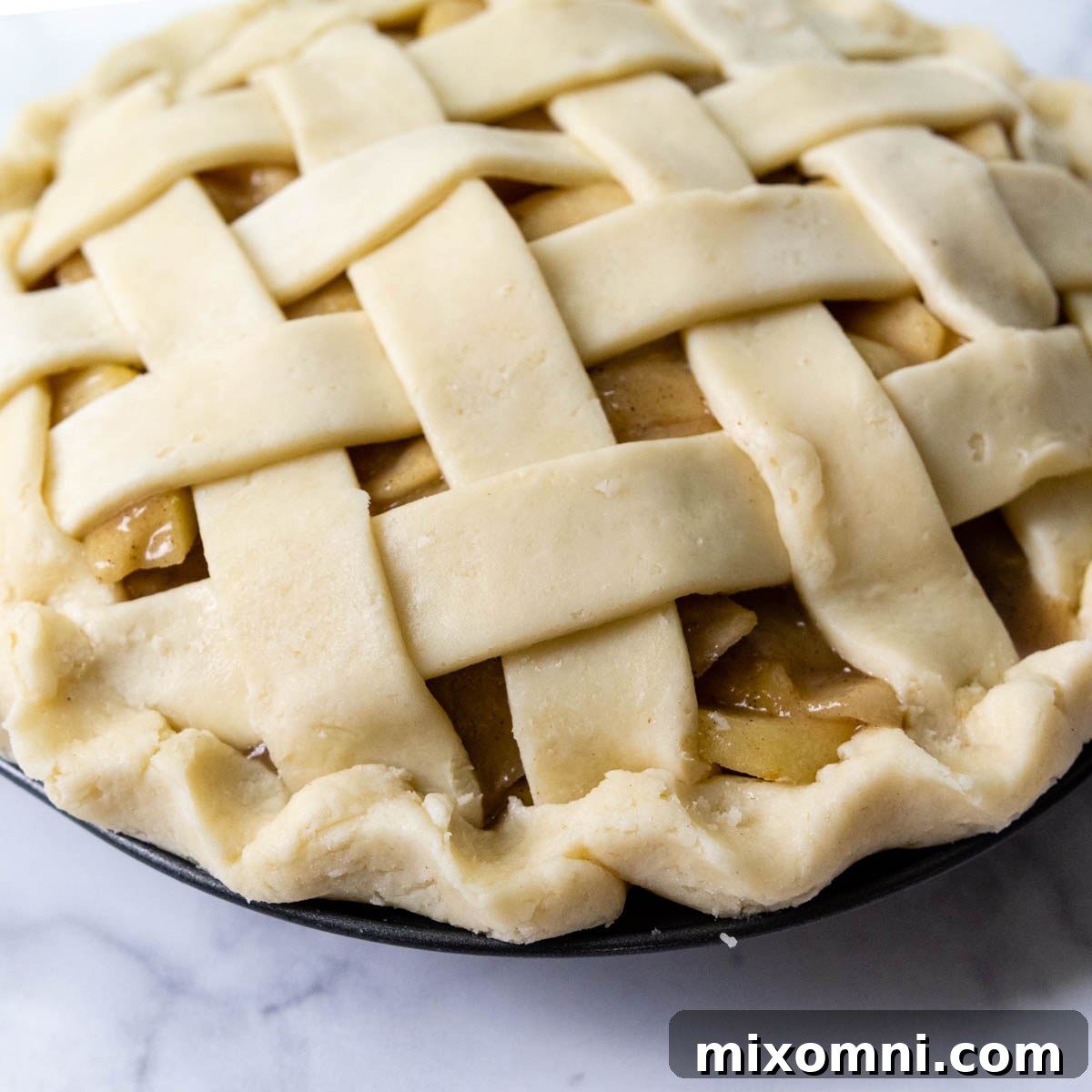 An unbaked apple pie with a finished lattice crust and a beautifully crimped, decorative edge.
