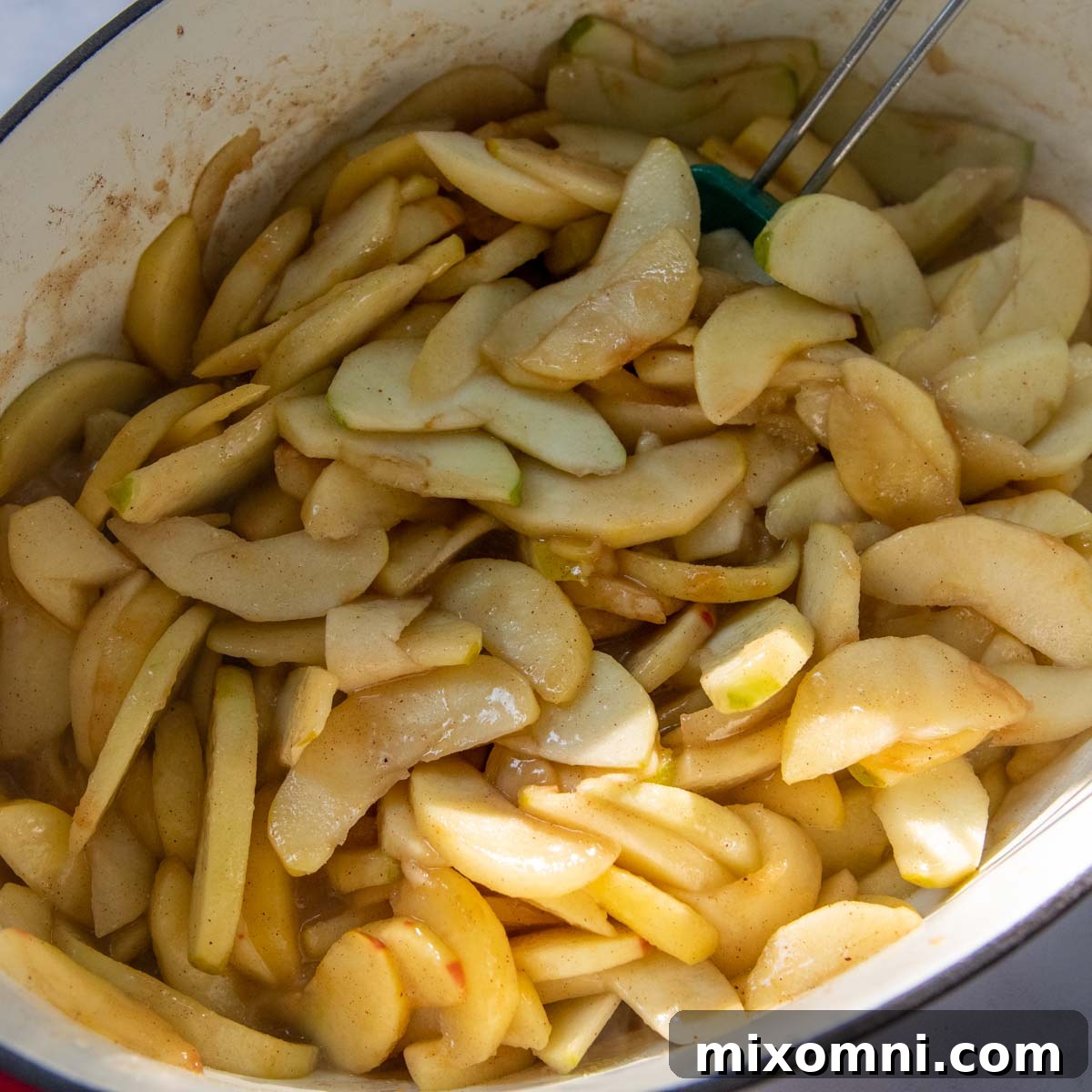 Partially cooked apple pie filling simmering in a Dutch oven, with vibrant spices and juices.
