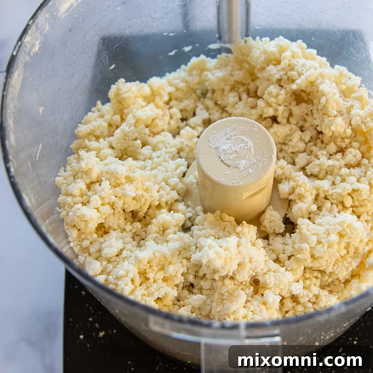 The gluten-free pie dough in a food processor, showing small clumps forming after liquids are added.
