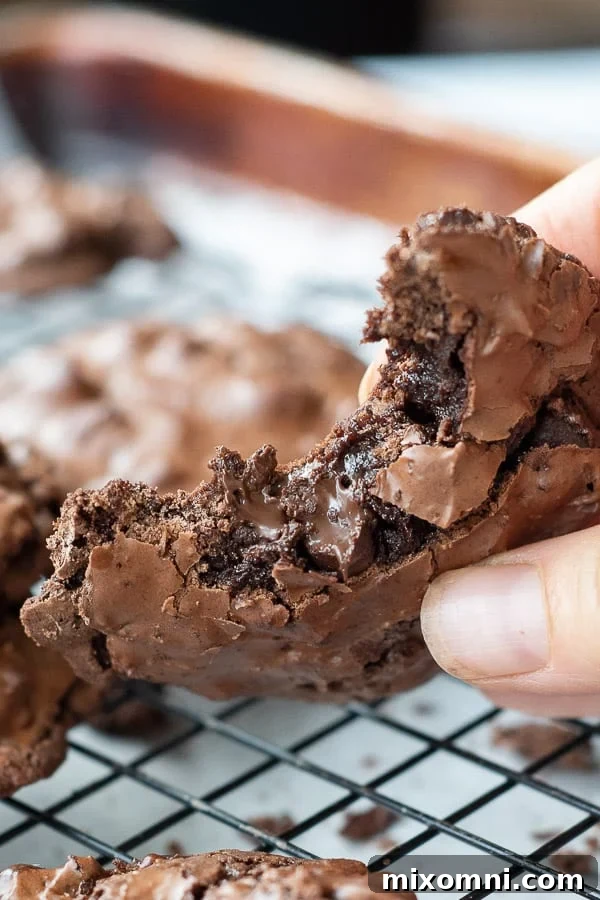 A perfectly baked, fudgy flourless chocolate cookie being held, with a bite taken out to reveal its soft, rich interior.