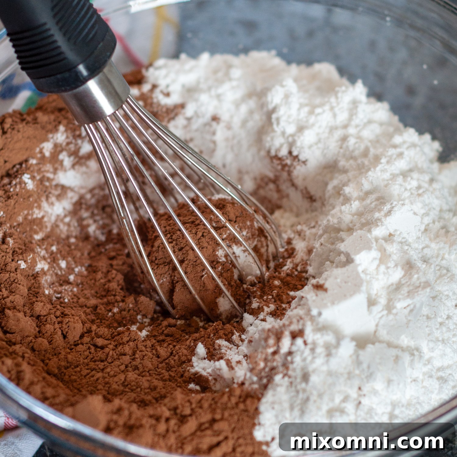 Dry ingredients, including cocoa powder, powdered sugar, and salt, are whisked together in a large mixing bowl.