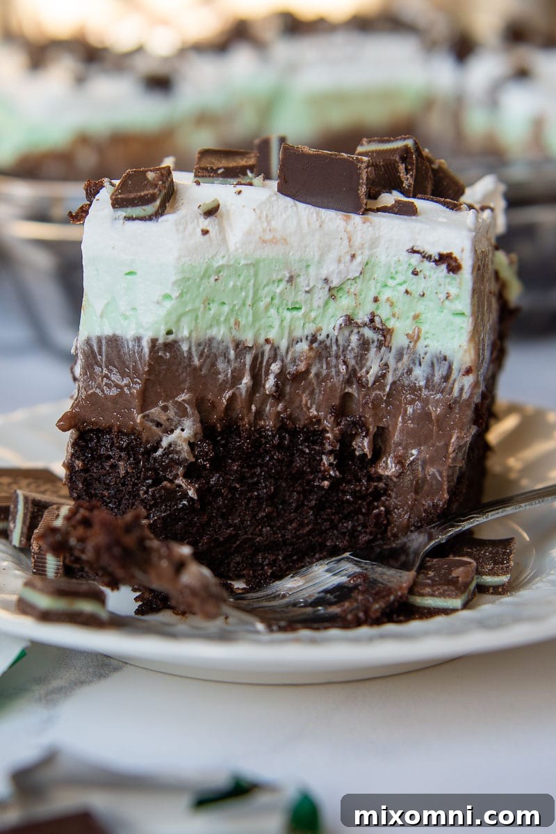 A large bite taken out of an Andes Mint Chocolate Pudding Poke Cake slice, with a fork resting on the white plate, highlighting the moist interior.