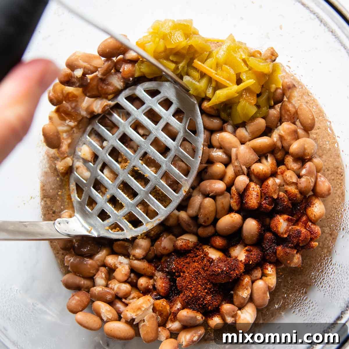 a potato masher mashing beans with seasonings.