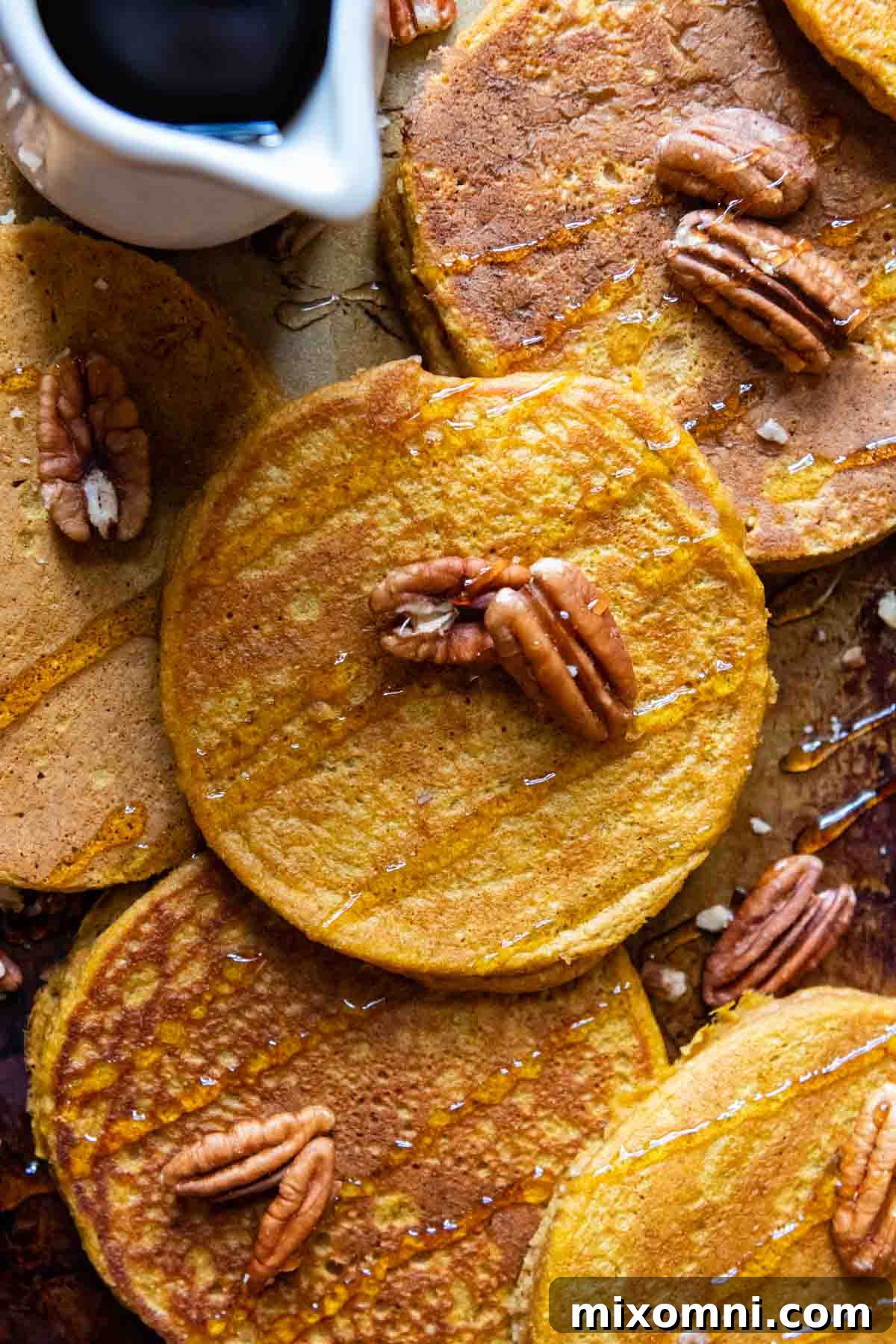 An inviting overhead shot of perfectly cooked pumpkin oatmeal pancakes on a pan, garnished with maple syrup and crunchy nuts, ready to be enjoyed.